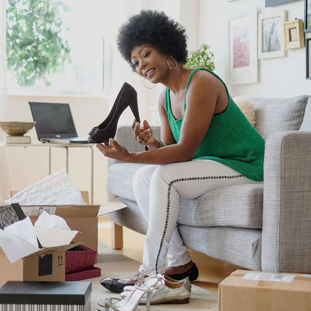 black woman in green top unboxing black shoes in her living room